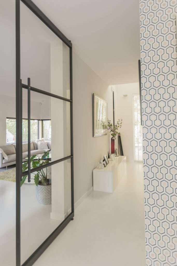 Stalen taatsdeur met slank zwart profiel die hal en woonkamer verbindt, met veel licht en een moderne, open uitstraling.