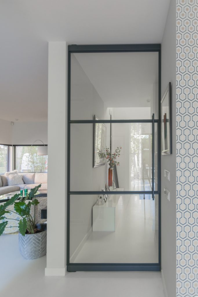 Stalen taatsdeur met slank zwart profiel die hal en woonkamer verbindt, met veel licht en een moderne, open uitstraling.