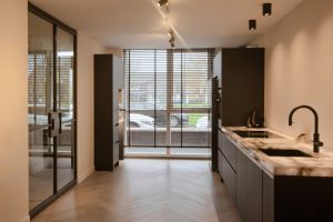 Stalen taatsdeuren met slanke messing profielen die woonkamer en trapruimte verbinden, met een moderne en lichte uitstraling.