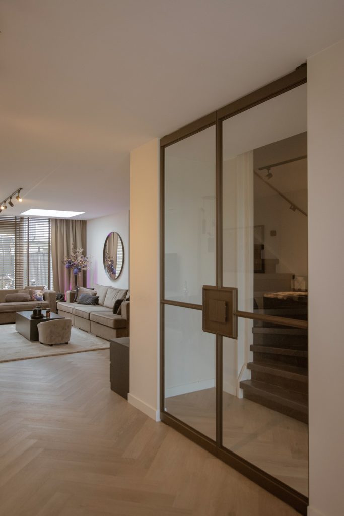 Stalen taatsdeuren met slanke messing profielen die woonkamer en trapruimte verbinden, met een moderne en lichte uitstraling.