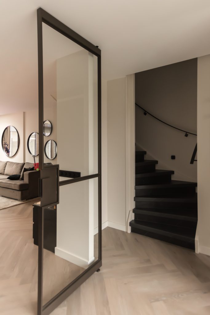 Stalen taatsdeuren met slanke messing profielen die woonkamer en trapruimte verbinden, met een moderne en lichte uitstraling.