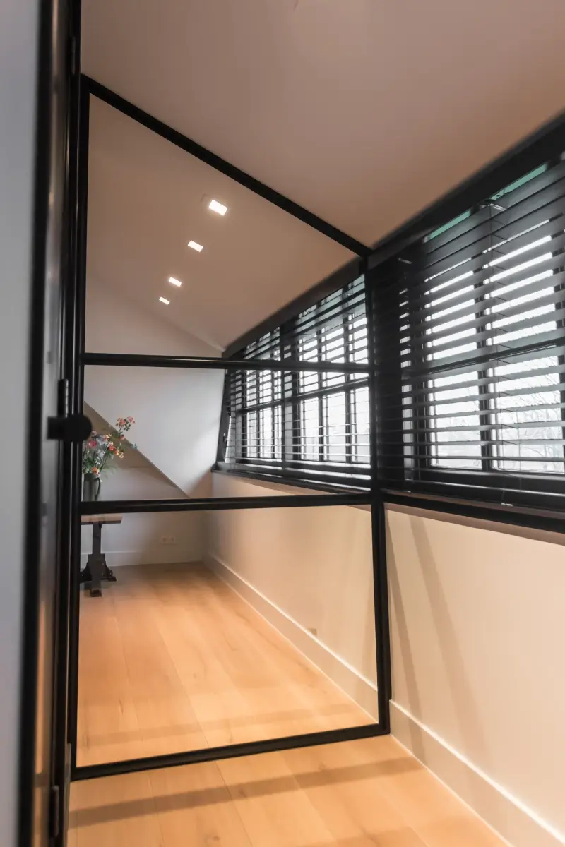 Stalen raampaneel met slank zwart profiel onder schuindak, met een moderne en lichte uitstraling.