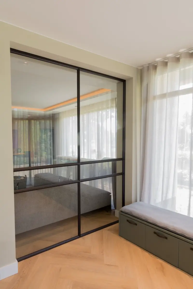Taatsdeur en raampaneel in modern interieur. Dit stalen raamkozijn is uitgevoerd in RAL 8022 in combinatie met grijs glas