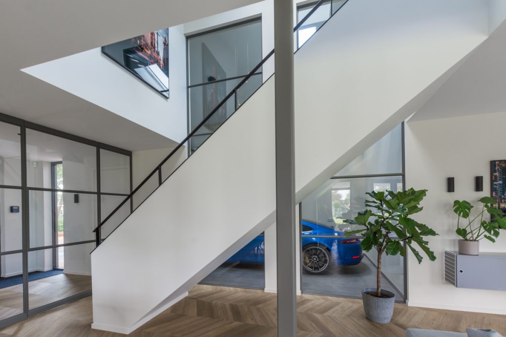 Stalen raampaneel tussen woning en garage met zicht op blauwe auto.
