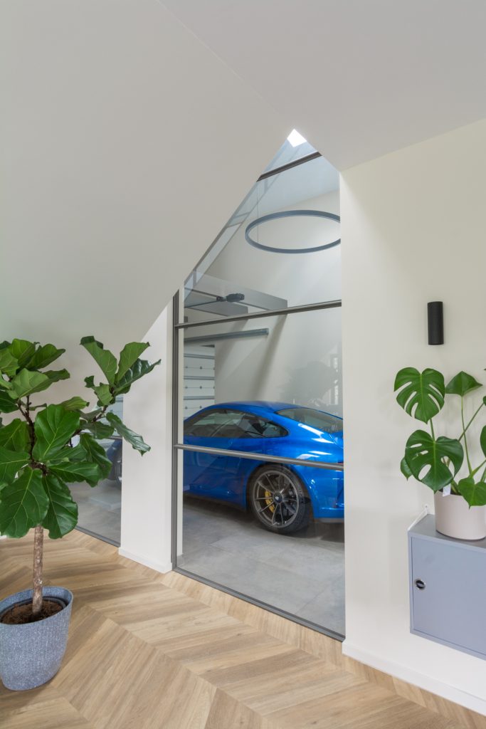 Stalen raampaneel tussen woning en garage met zicht op blauwe auto.