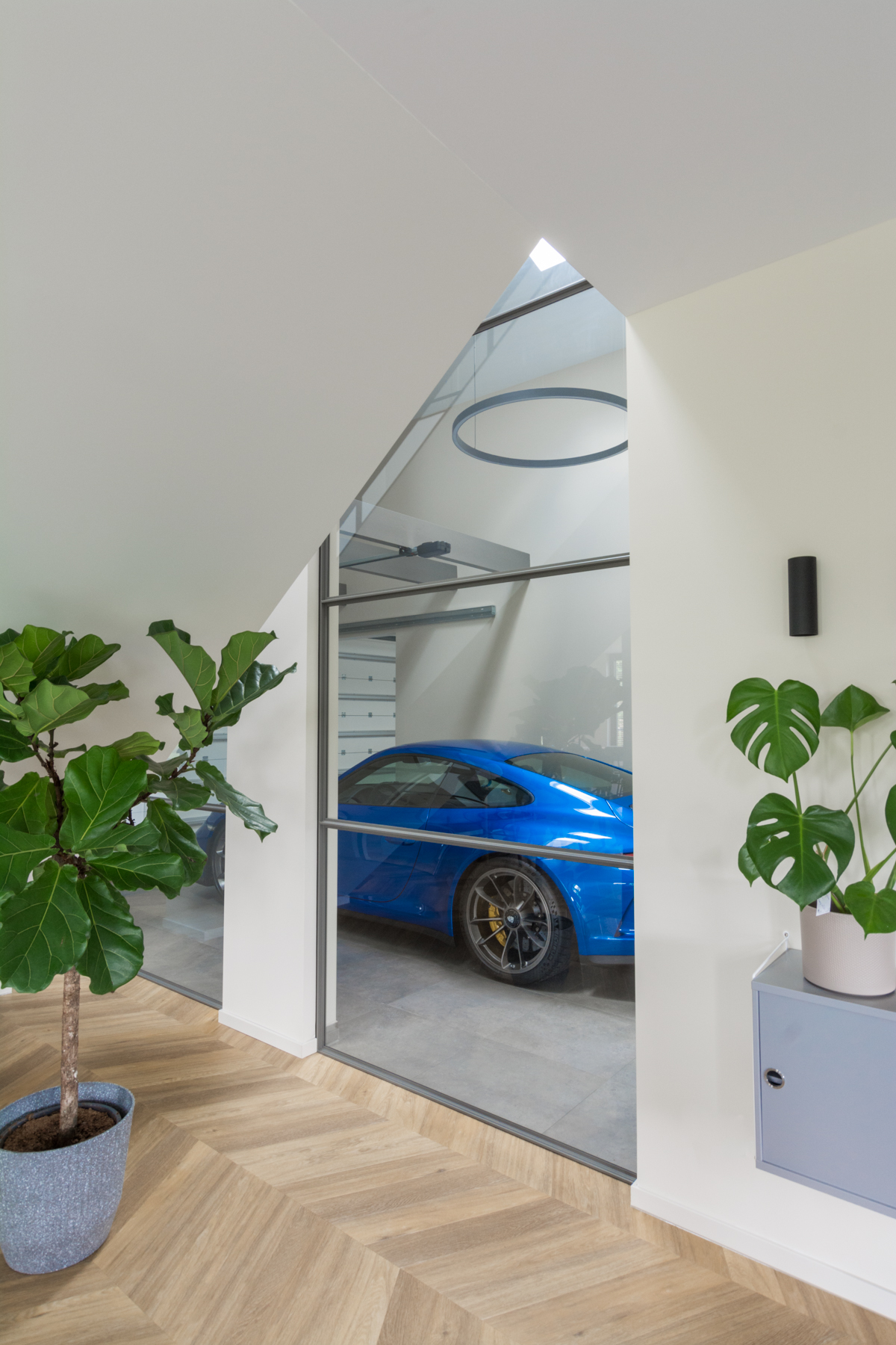 Stalen raampaneel tussen woning en garage met zicht op blauwe auto.