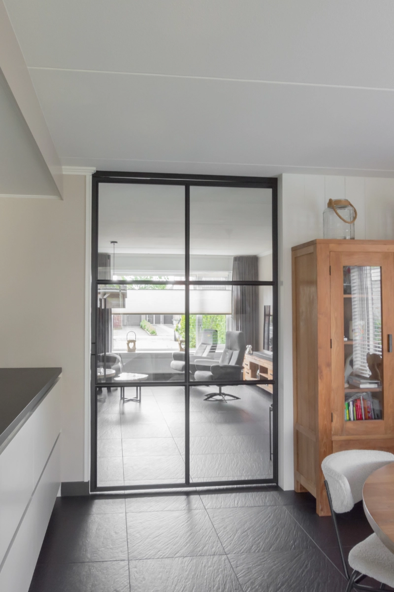 Minimalistisch interieur met zwart stalen schuifdeur tussen woonkamer en keuken.