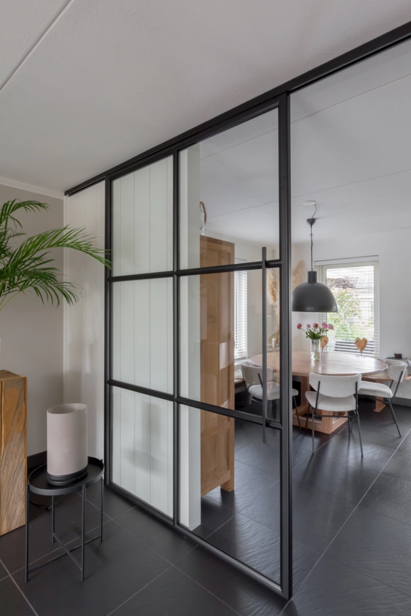 Minimalistisch interieur met zwart stalen schuifdeur tussen woonkamer en keuken.