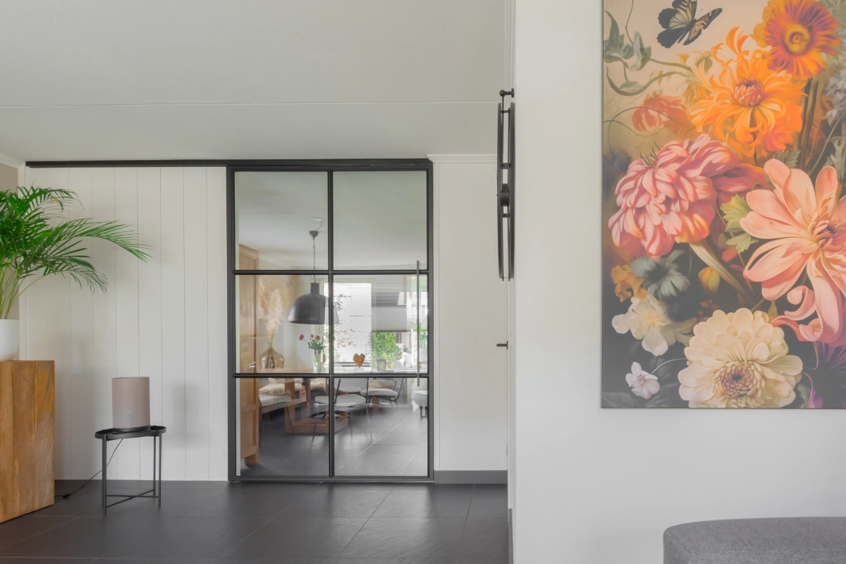 Minimalistisch interieur met zwart stalen schuifdeur tussen woonkamer en keuken.
