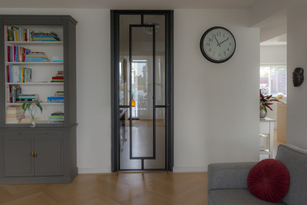 Stalen scharnierdeur met kozijnbekleding uitgevoerd in RAL 9005 gitzwart toegepast in een moderne leefruimte met doorkijk naar de hal.
