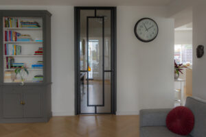 Stalen scharnierdeur met kozijnbekleding uitgevoerd in RAL 9005 gitzwart toegepast in een moderne leefruimte met doorkijk naar de hal.