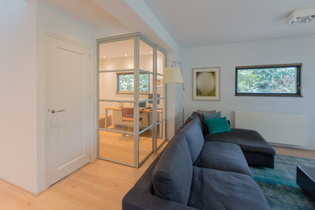 Stalen schuifdeuren in hoekopstelling met raampaneel in moderne woonkamer.
