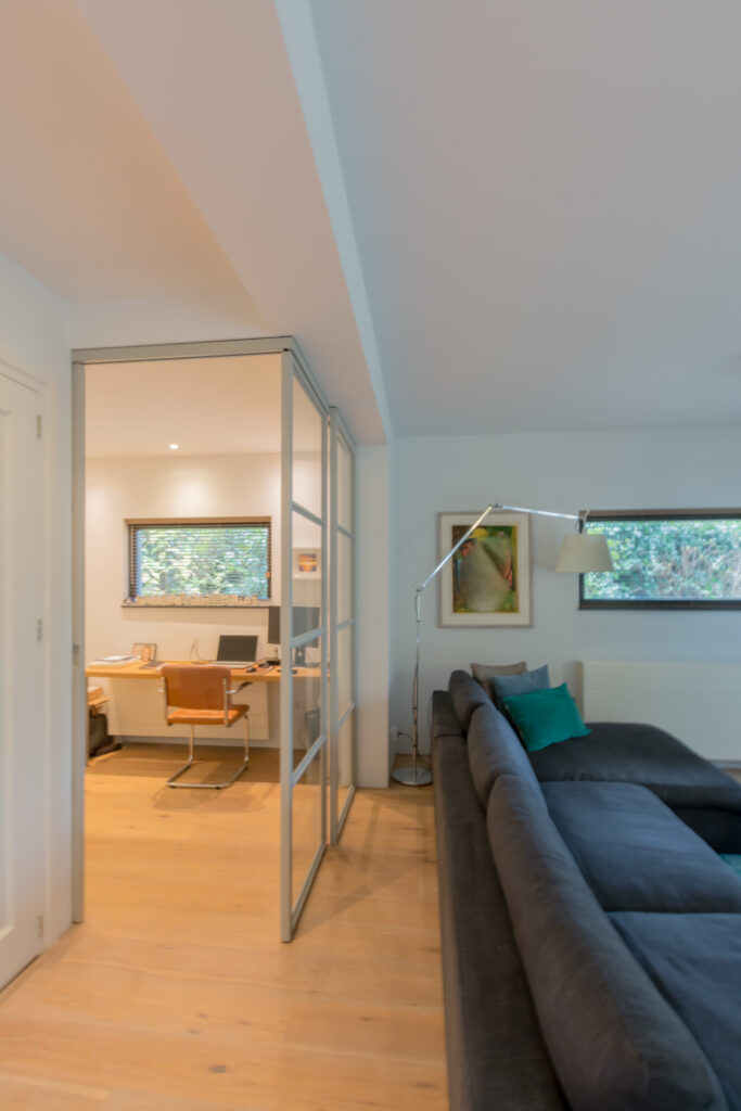 Stalen schuifdeuren in hoekopstelling met raampaneel in moderne woonkamer.