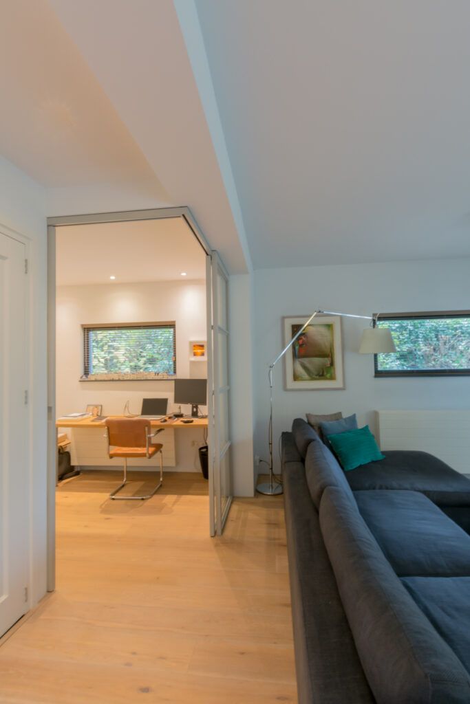 Stalen schuifdeuren in hoekopstelling met raampaneel in moderne woonkamer.