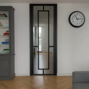 Stalen scharnierdeur met kozijnbekleding uitgevoerd in RAL 9005 gitzwart toegepast in een moderne leefruimte met doorkijk naar de hal.