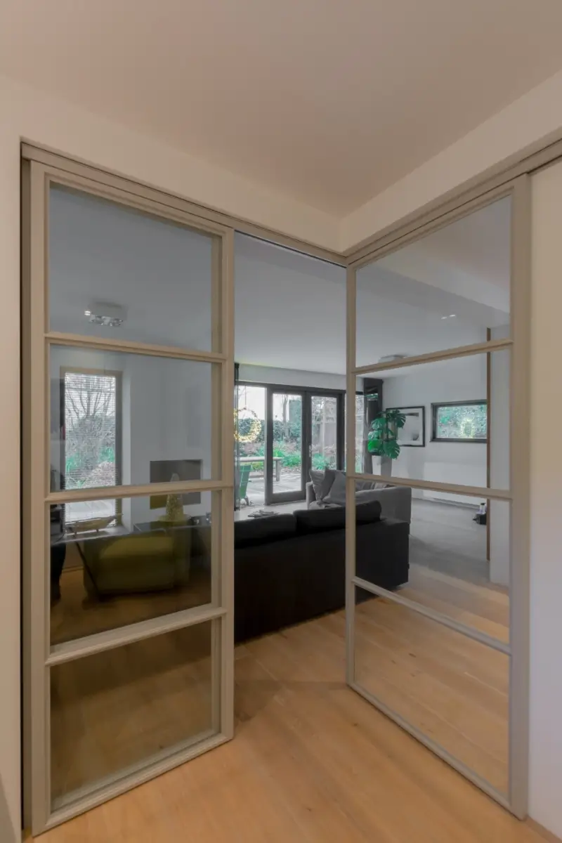 Stalen schuifdeuren in hoekopstelling met raampaneel in moderne woonkamer.
