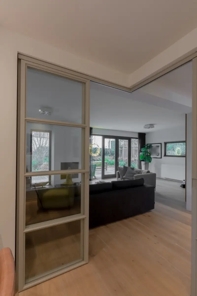Stalen schuifdeuren in hoekopstelling met raampaneel in moderne woonkamer.