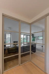 Stalen schuifdeuren in hoekopstelling met raampaneel in moderne woonkamer.