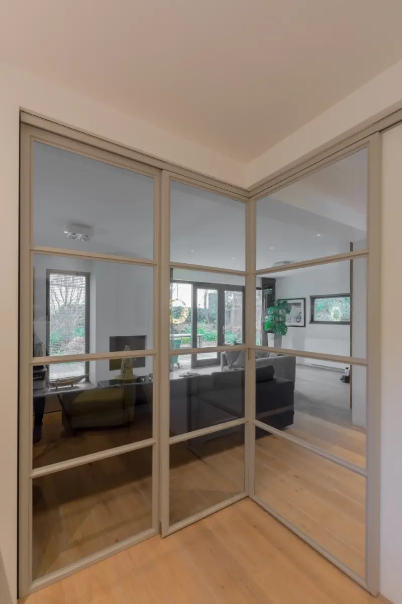 Stalen schuifdeuren in hoekopstelling met raampaneel in moderne woonkamer.