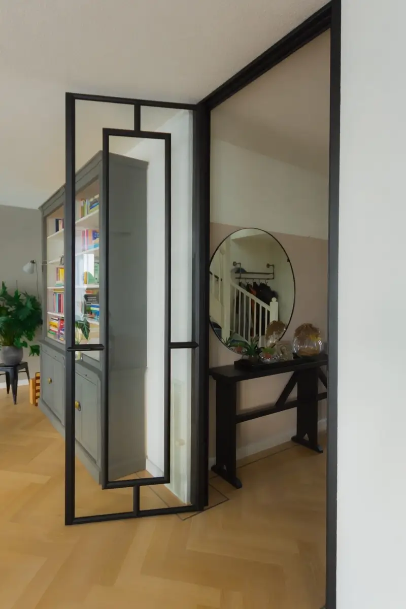 Stalen scharnierdeur met kozijnbekleding uitgevoerd in RAL 9005 gitzwart toegepast in een moderne leefruimte met doorkijk naar de hal.