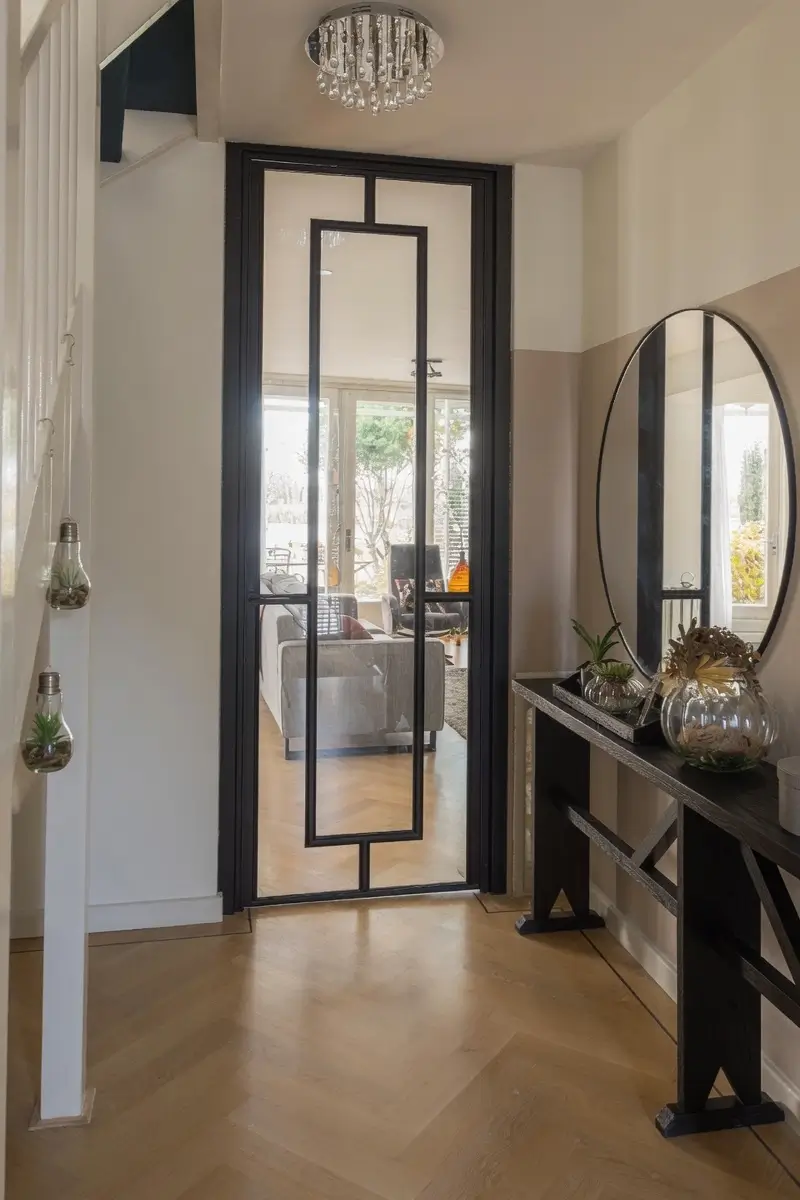 Stalen scharnierdeur met kozijnbekleding uitgevoerd in RAL 9005 gitzwart toegepast in een moderne leefruimte met doorkijk naar de hal.