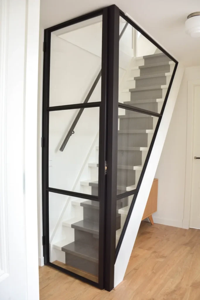 Stalen scharnierdeur met rolslot en raampaneel op maat als trapafscheiding in modern interieur